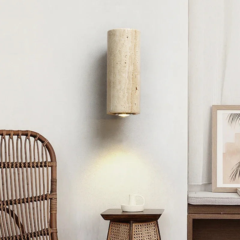 Round travertine sconce lit against a pale wall