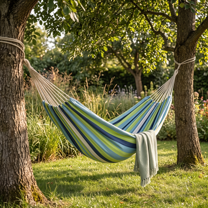 Striped canvas hammock slung between two trees in a summer garden